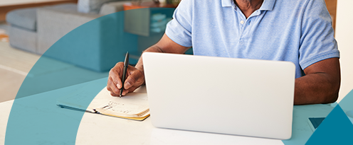 Man on laptop making notes on a notepad